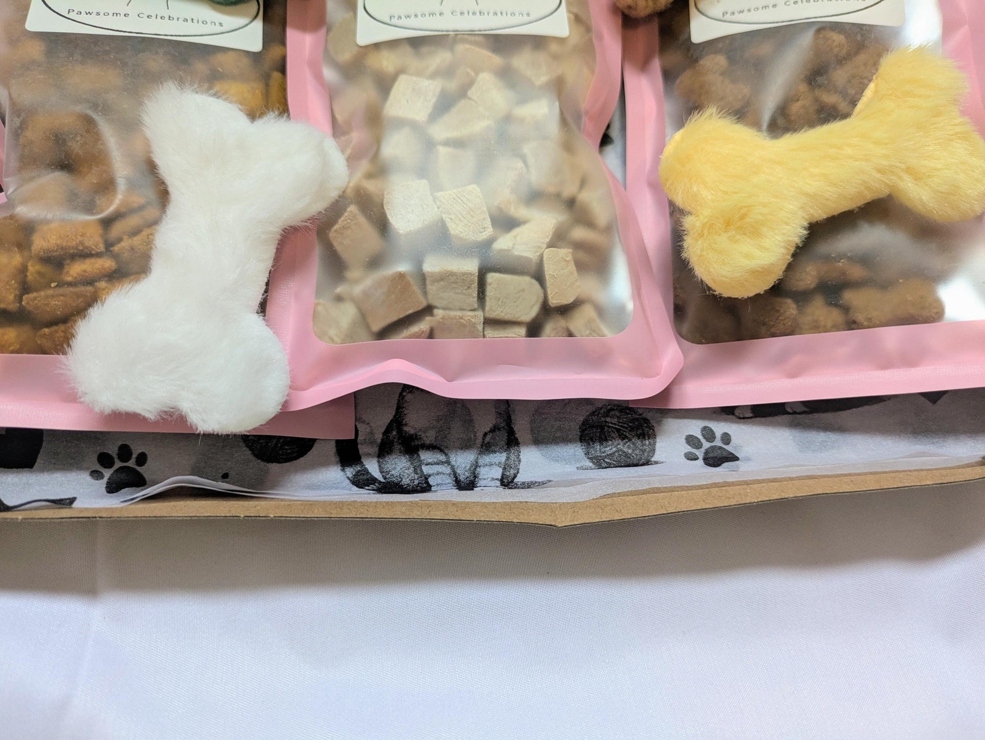 Medium cat treat box with assorted bone-shaped and cube cat snacks in clear bags, pink tray, paw print box lining.
