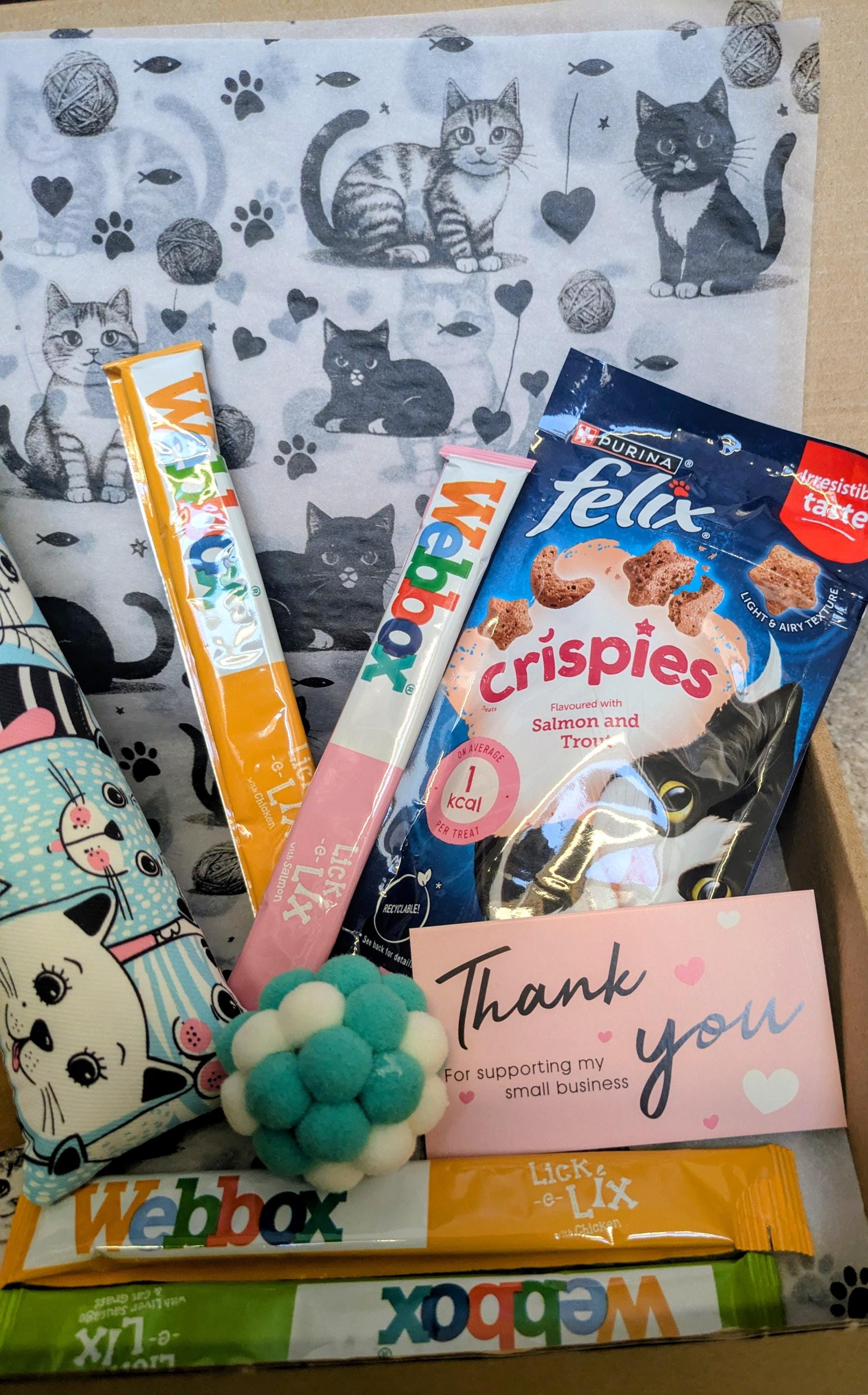 Personalized cat treat box with catnip kicker toy, cat snacks, and thank you card on patterned cat-print fabric background.