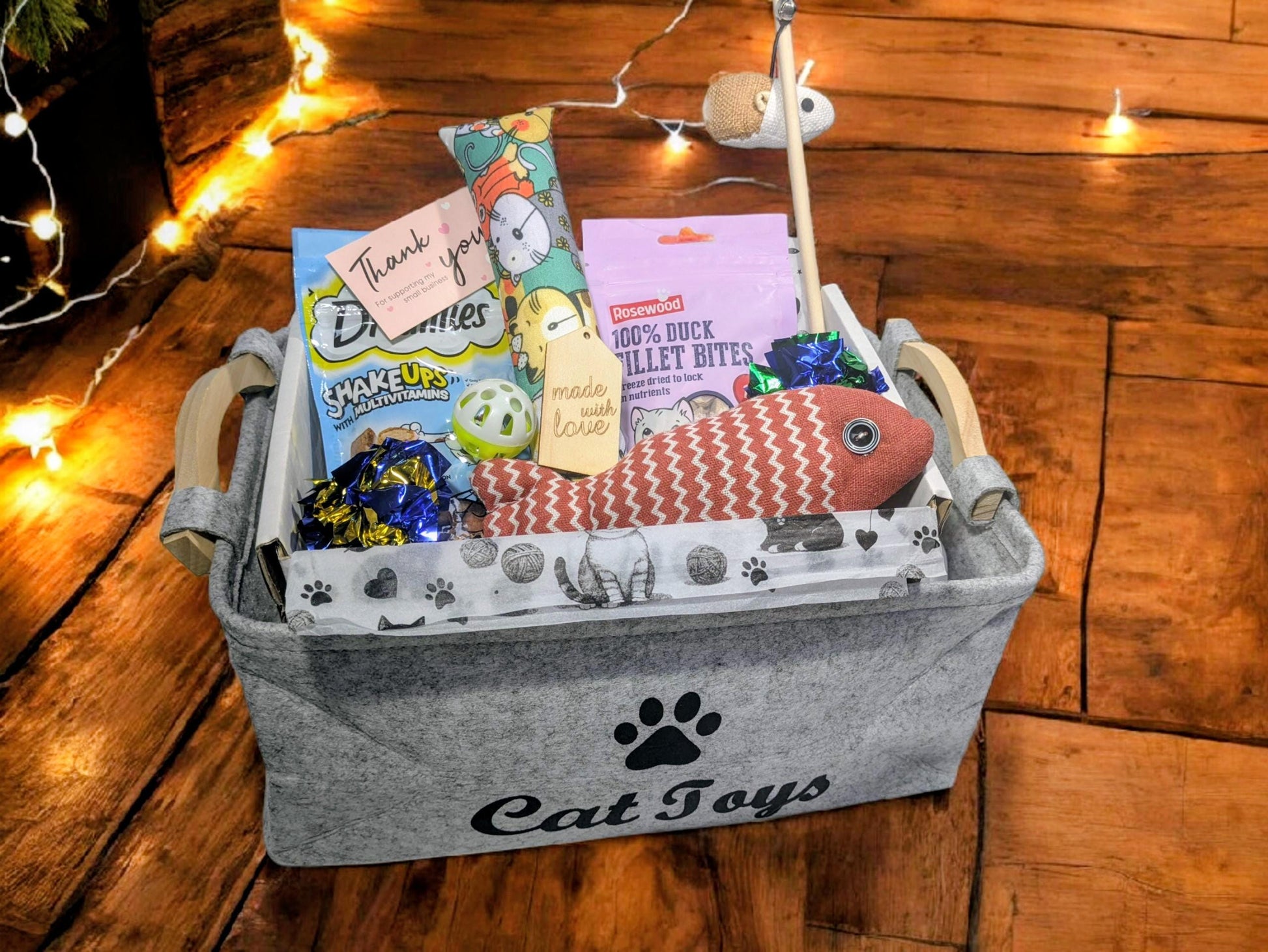 Grey felt cat hamper with paw print and "Cat Joy" text, filled with colorful cat treats, toys, and a pink fish toy.