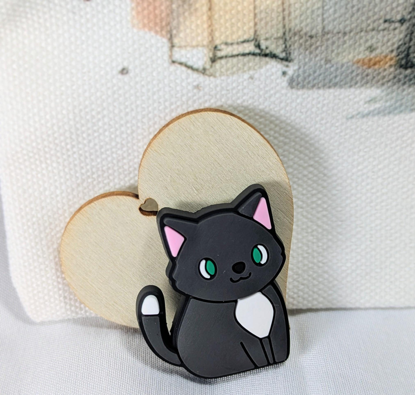 Black cat enamel pin with green eyes and white chest on wooden heart-shaped backing.