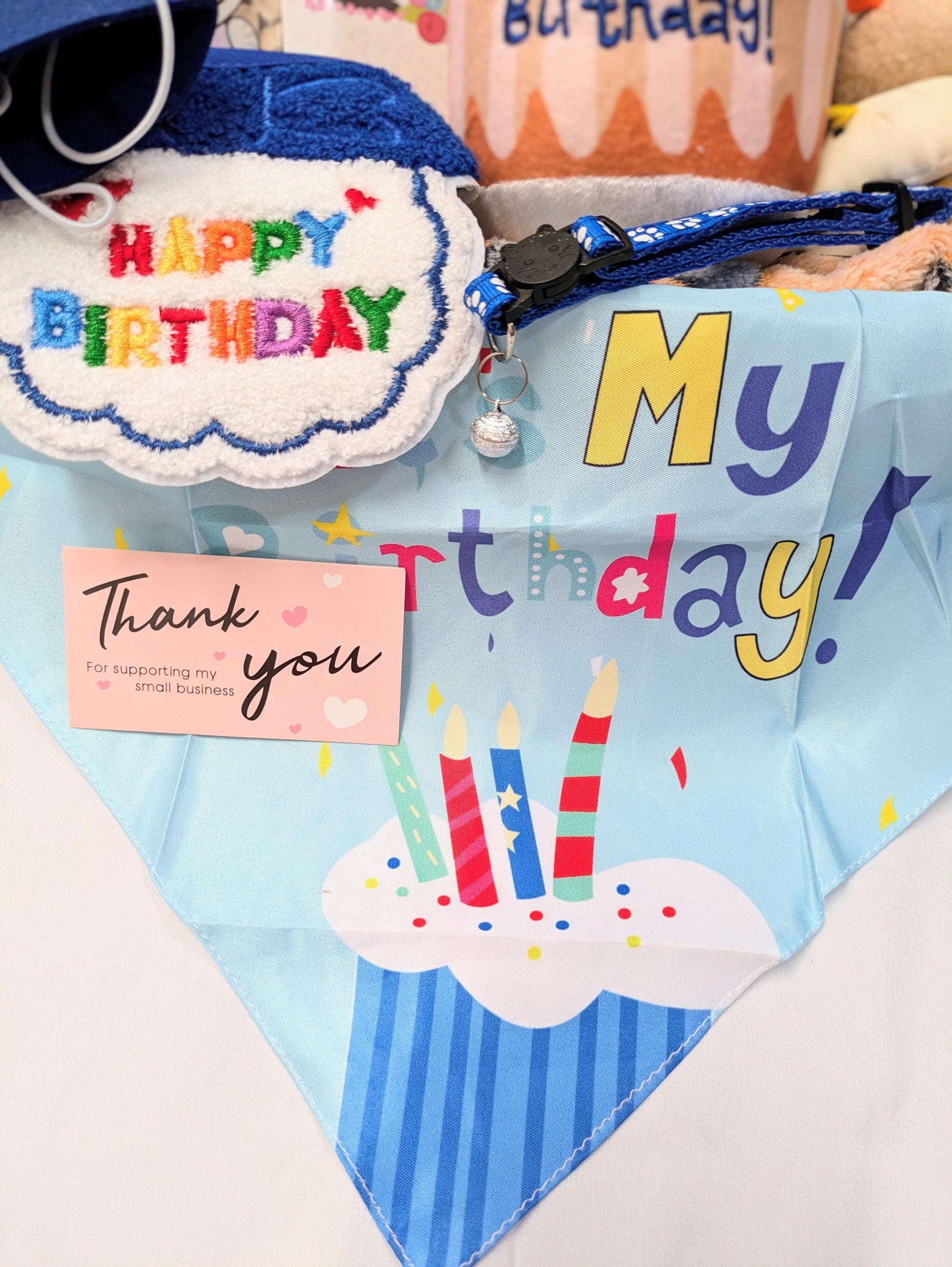 Colorful cat bandana with "My Birthday" text and cupcake design with candles, birthday-themed cat toys and treats in.