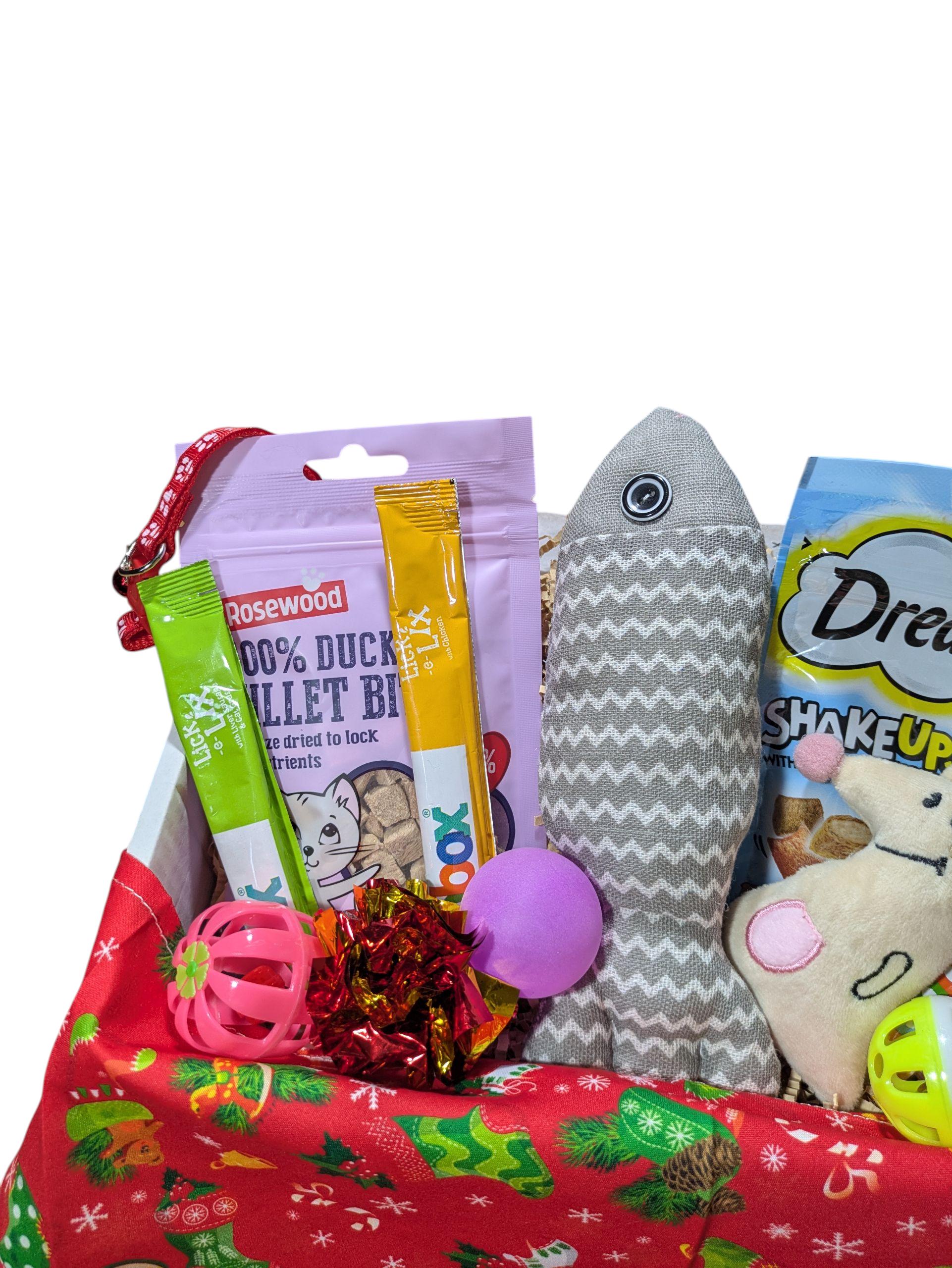 Red Christmas-themed cat treat box filled with duck fillet bites, fish-shaped toy, pink ball, and assorted cat treats.
