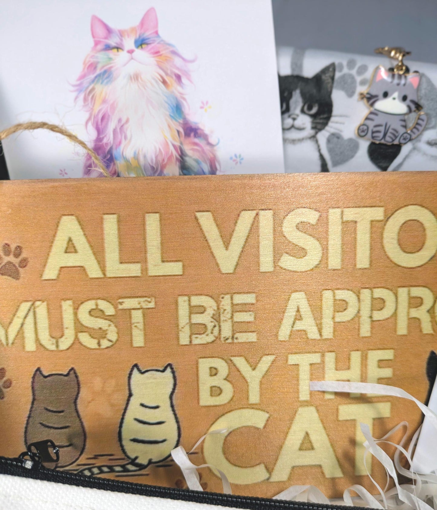 Wooden sign with gold letters reading "All visitors must be approved by the cat" and three illustrated cats sitting at the.