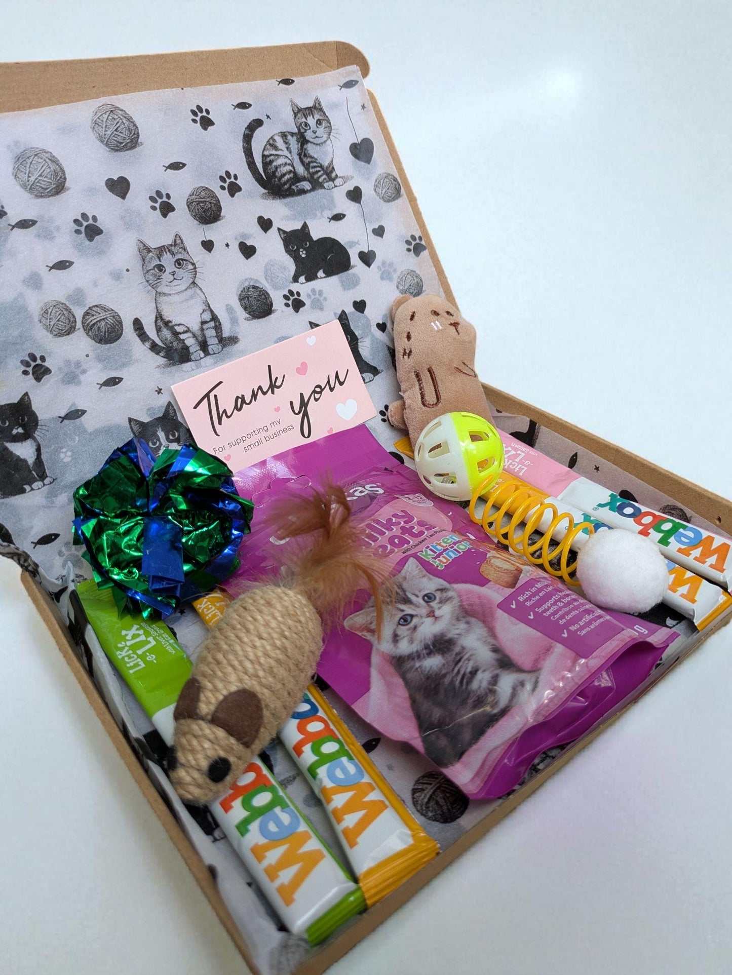 Open letterbox gift containing kitten treats, toys, and a thank you card with cat illustrations.