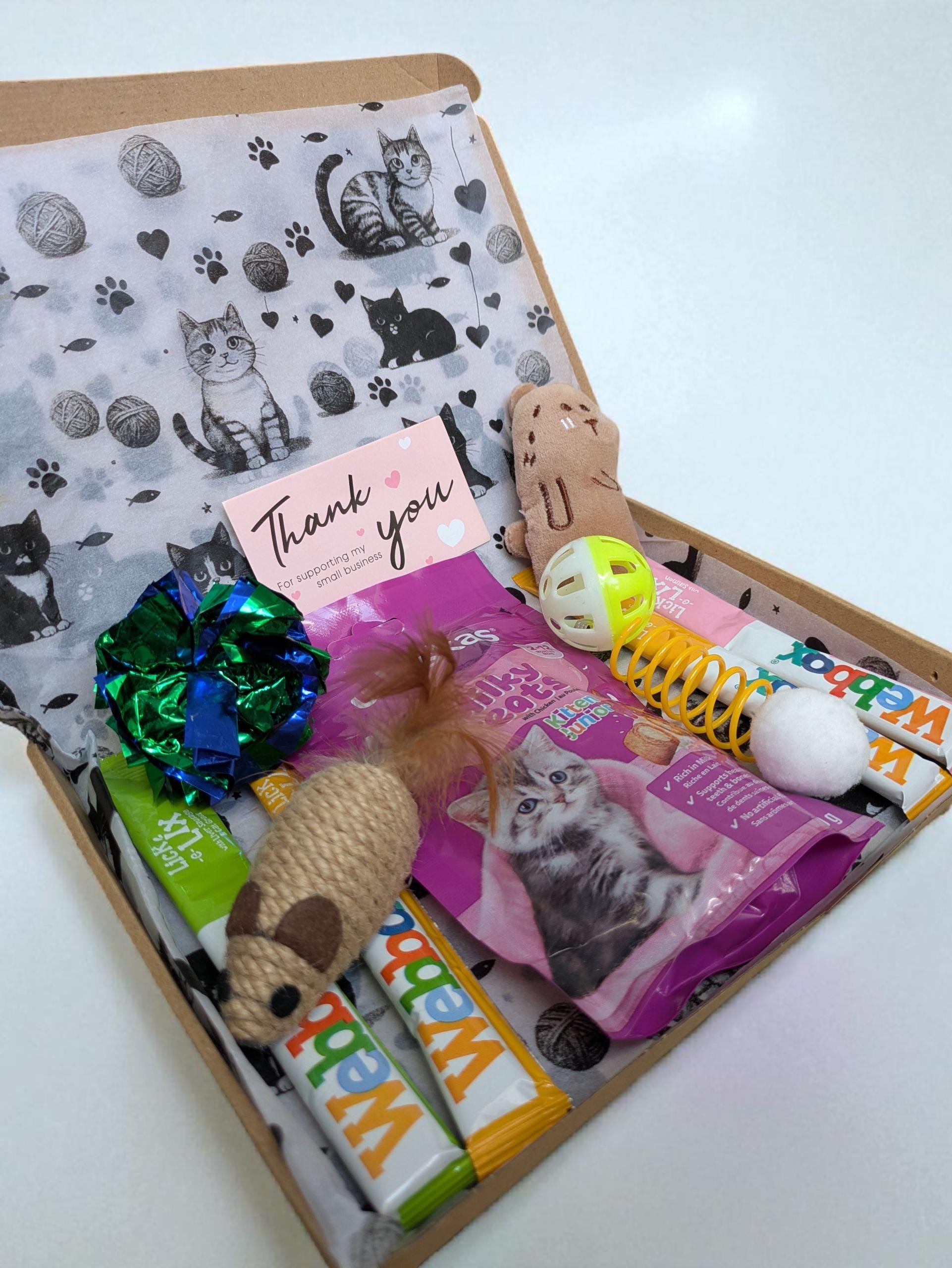 Open letterbox gift containing kitten treats, toys, and a thank you card with cat illustrations.