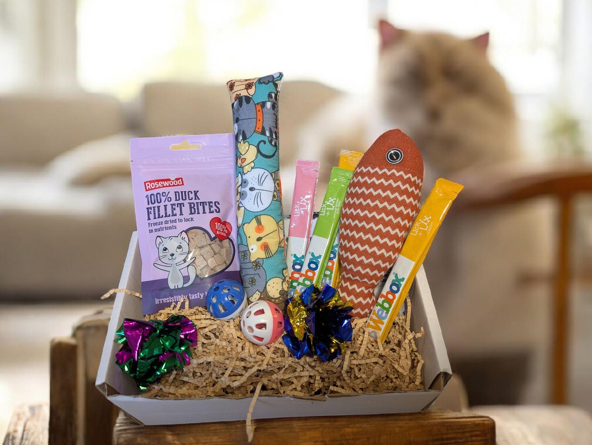 Personalised white cat treat box with colorful catnip toys, feather wand, and sachet of fish fillet bites on natural straw.