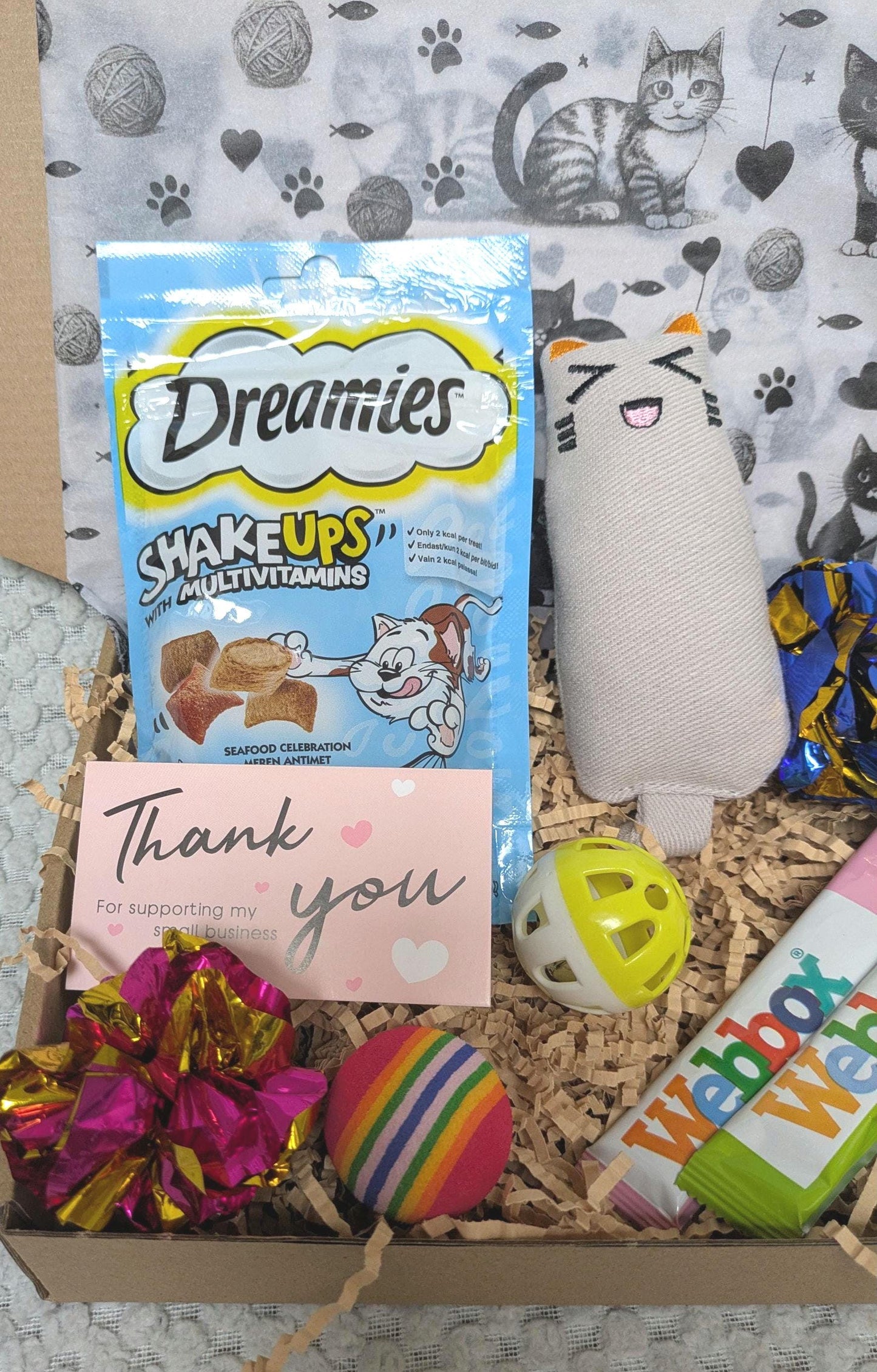 Cat treat box with Dreamies Shake Ups pouch, plush cat toy, colorful ball toys, and thank you card in shredded paper.
