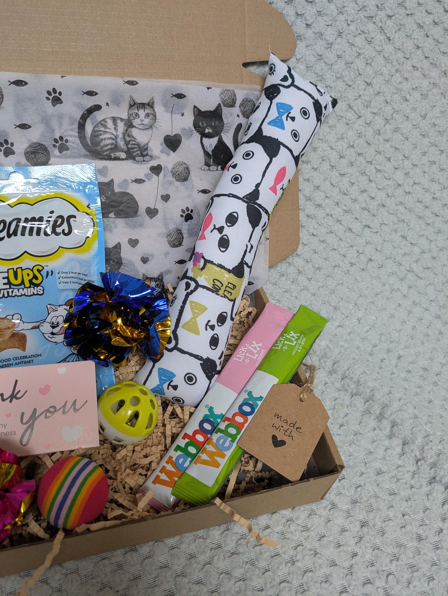 Open cardboard gift box with catnip kicker toy, premium cat treats, colorful balls, and thank you card.