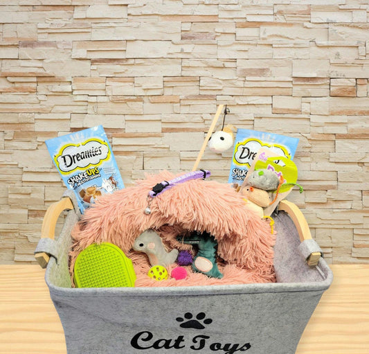 Grey fabric cat toy box filled with a pink fluffy bed, assorted plush toys, and colorful cat treats.