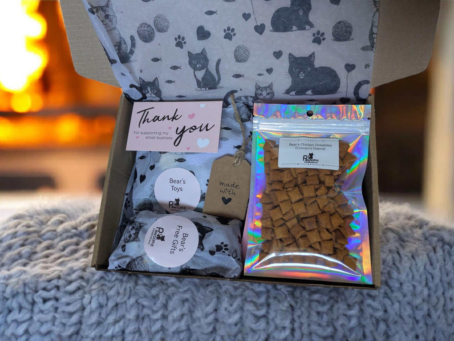 Small cardboard cat treat box with cat-patterned interior, catnip kicker toy, and holographic bag of treats.