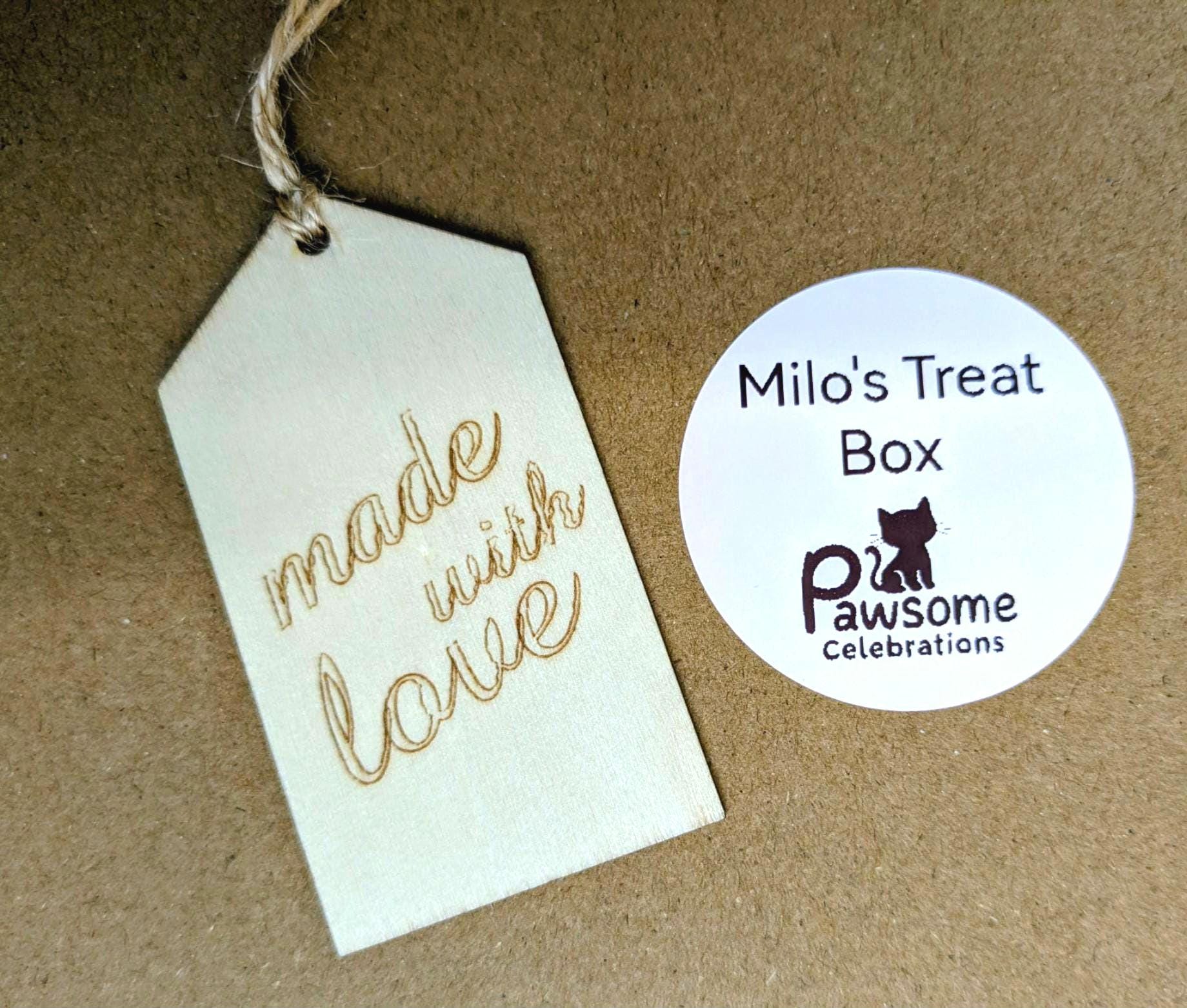 Wooden tag engraved with "made with love" and personalized round label for Milo's Treat Box by Pawsome Celebrations on brown .