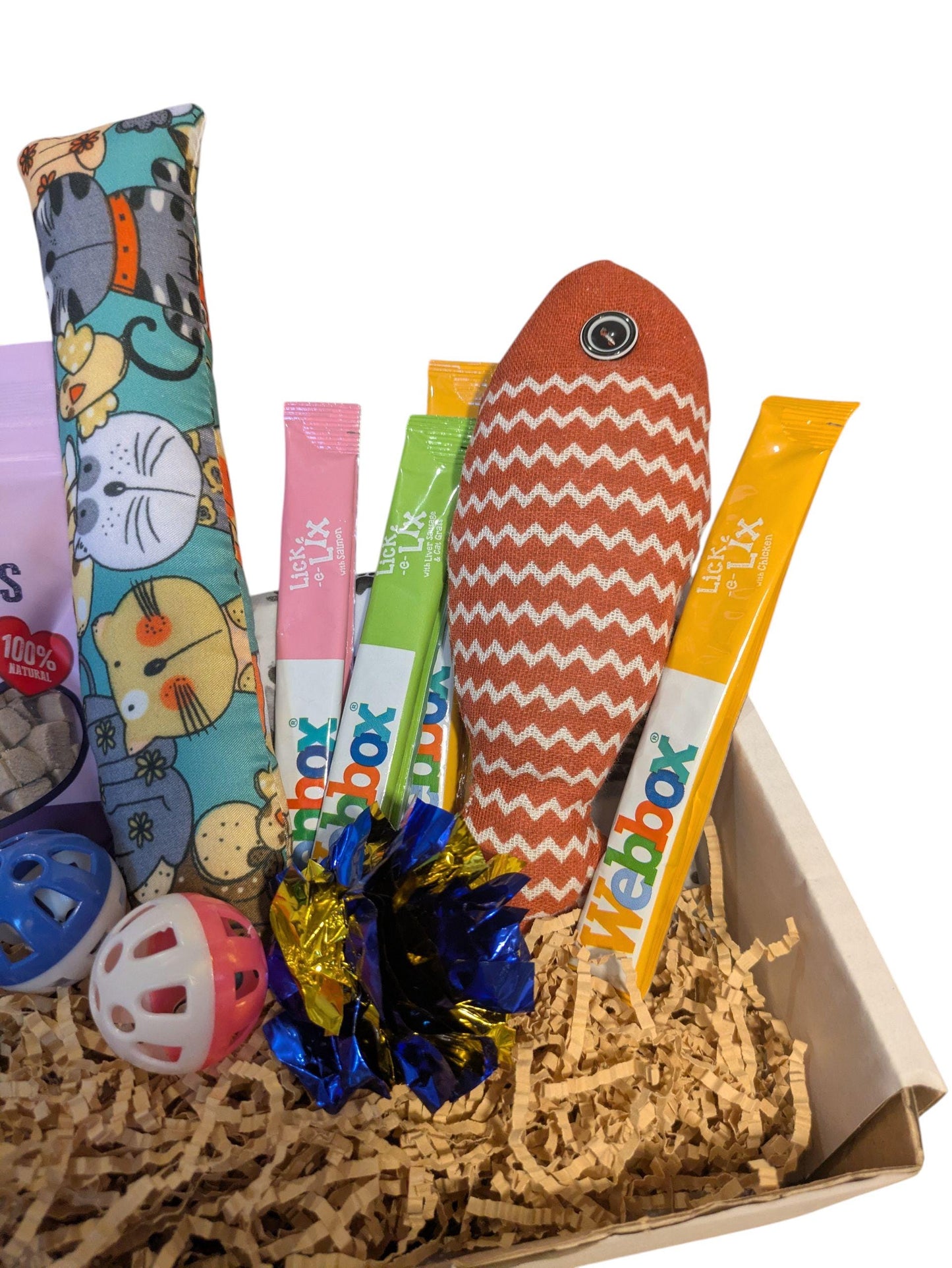 Wooden box with orange fish-shaped catnip toy, colorful treat sticks, and blue ball in shredded paper.