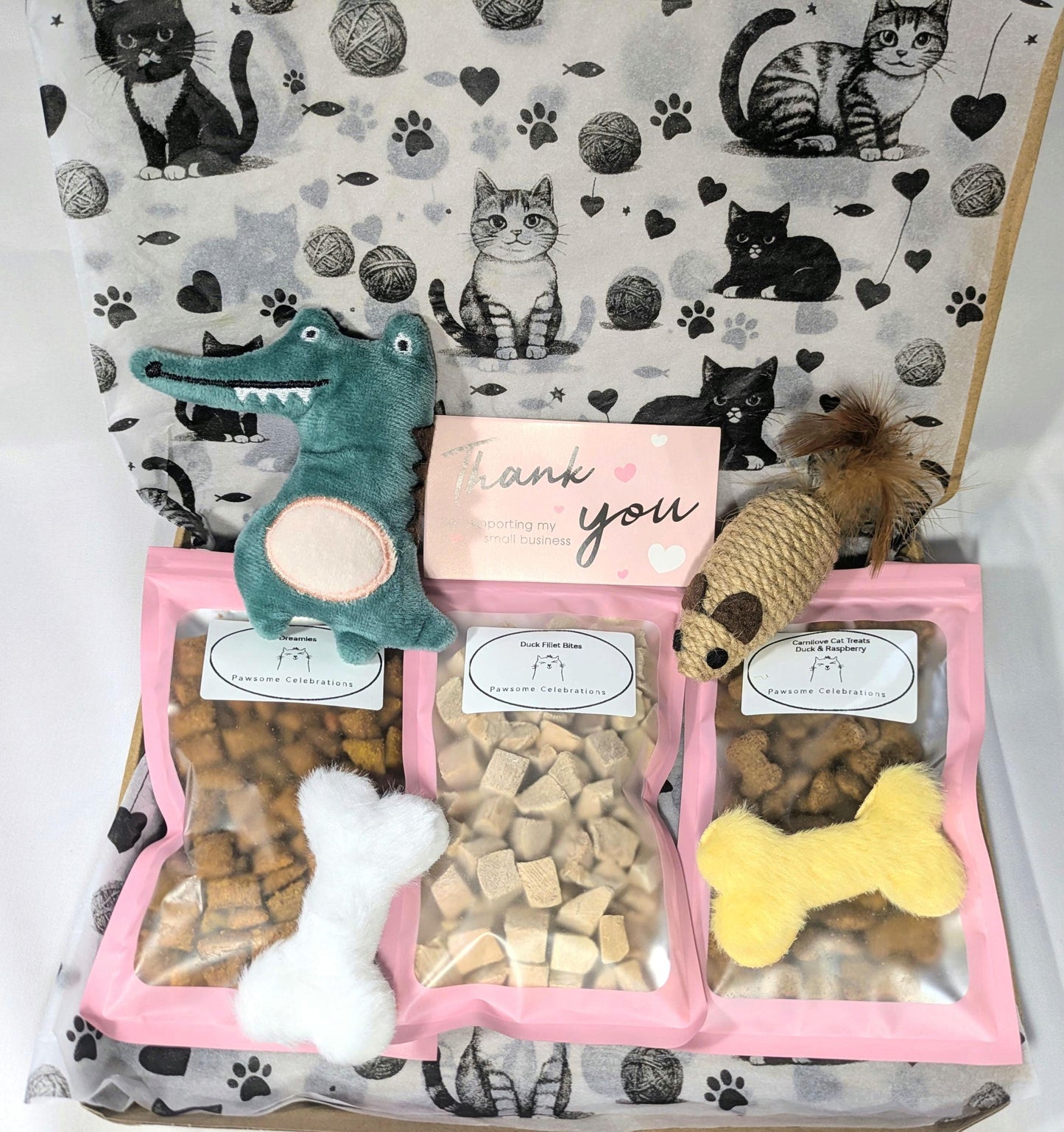 Pink cat treat box with three compartments holding bone-shaped treats, plush crocodile, sisal mouse, and a thank you card,.