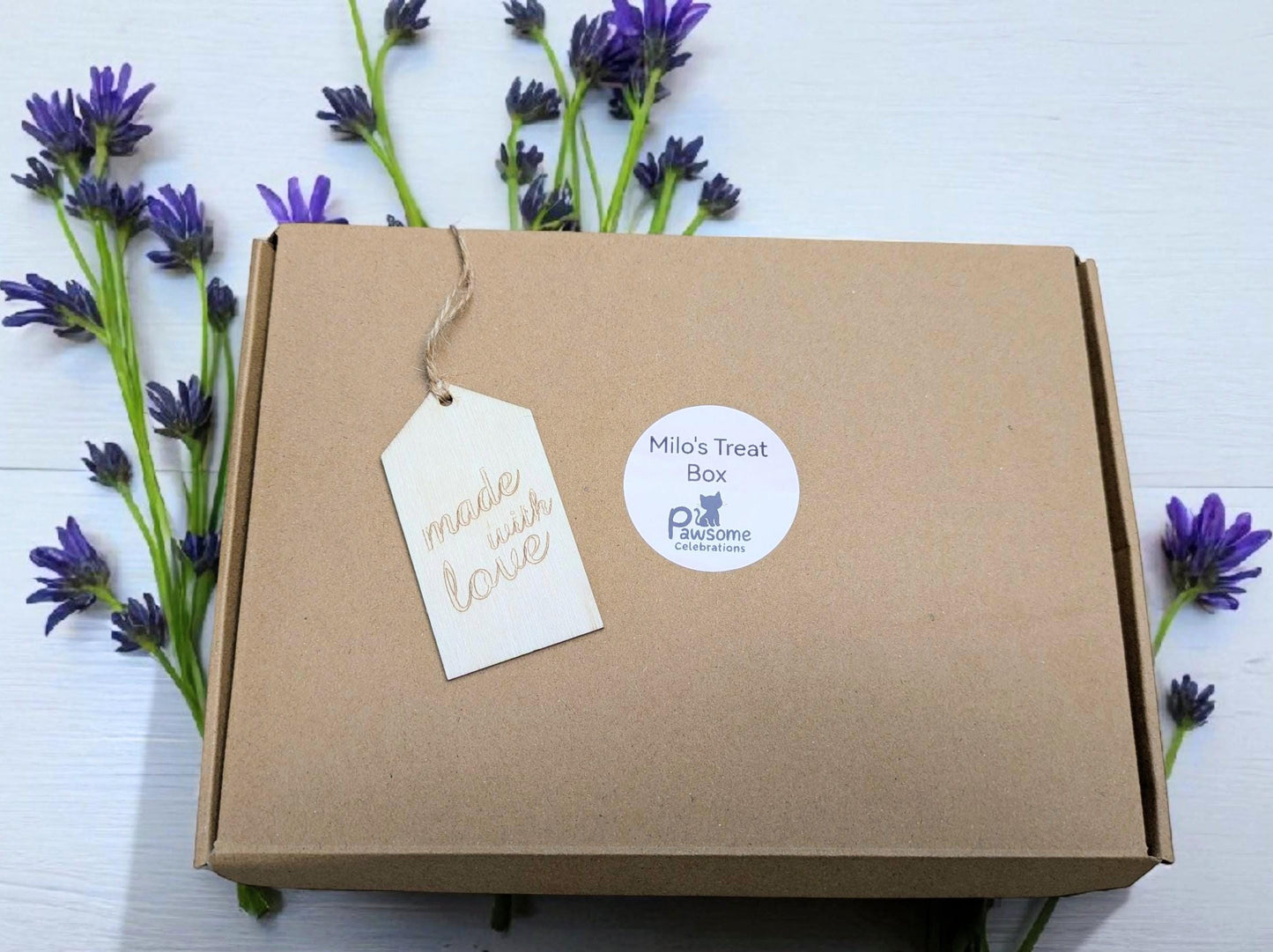 Brown cardboard cat treat box with white tags, surrounded by purple lavender flowers.