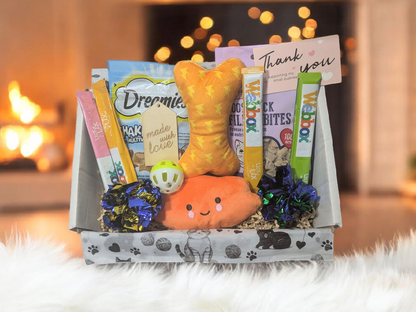 Cat toy and treat gift box with orange fish plush, ball, Dreamies treats, and thank you card in eco-friendly paw print.