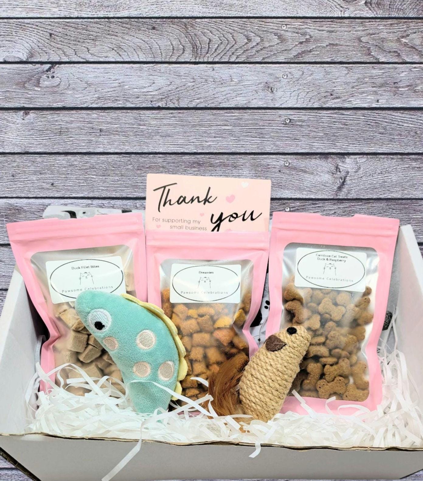 Medium cat treat box with three pink-sealed bags of treats, a mouse toy, a fish toy, and a thank you card.