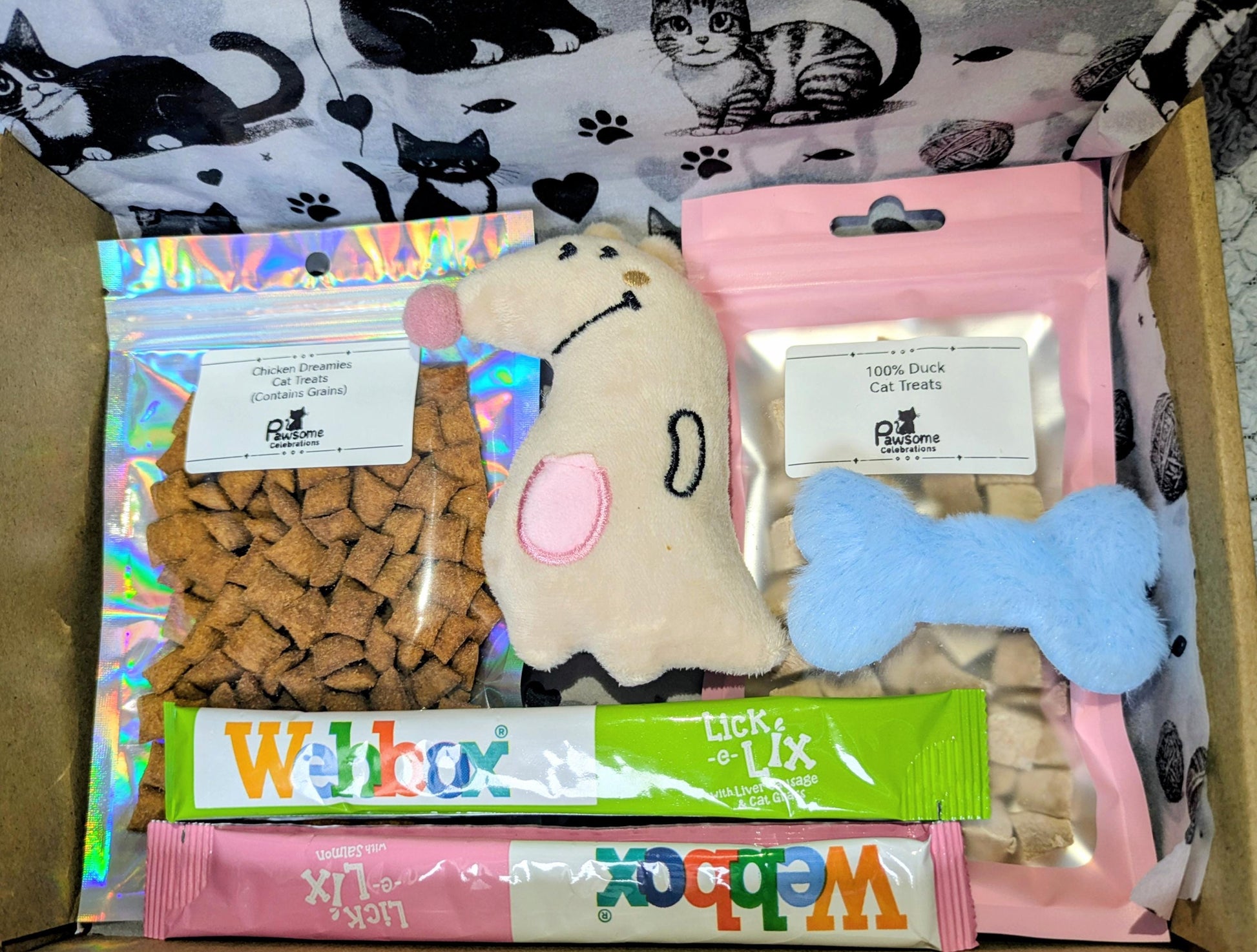 Small cat treat box with heart-shaped kibble, plush mouse toy, blue bone toy, and green and pink cat treat sticks in pink.