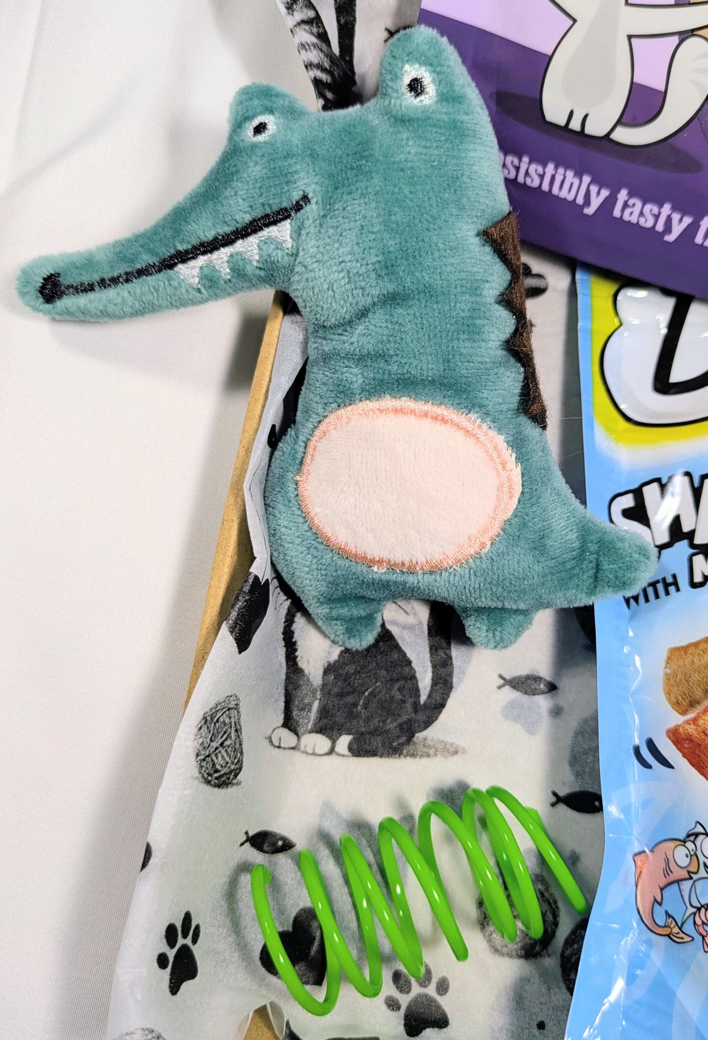 Soft green crocodile cat toy with embroidered details and a spring toy on a paw-print blanket.