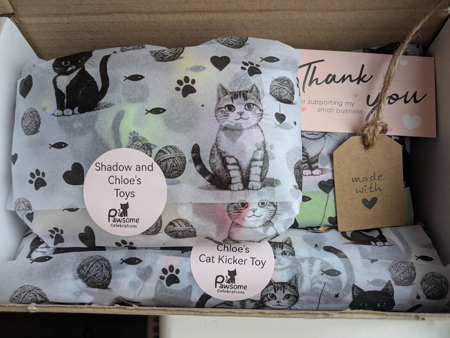 Open cardboard box with cat-themed tissue paper, thank you card, and labelled cat toys inside.