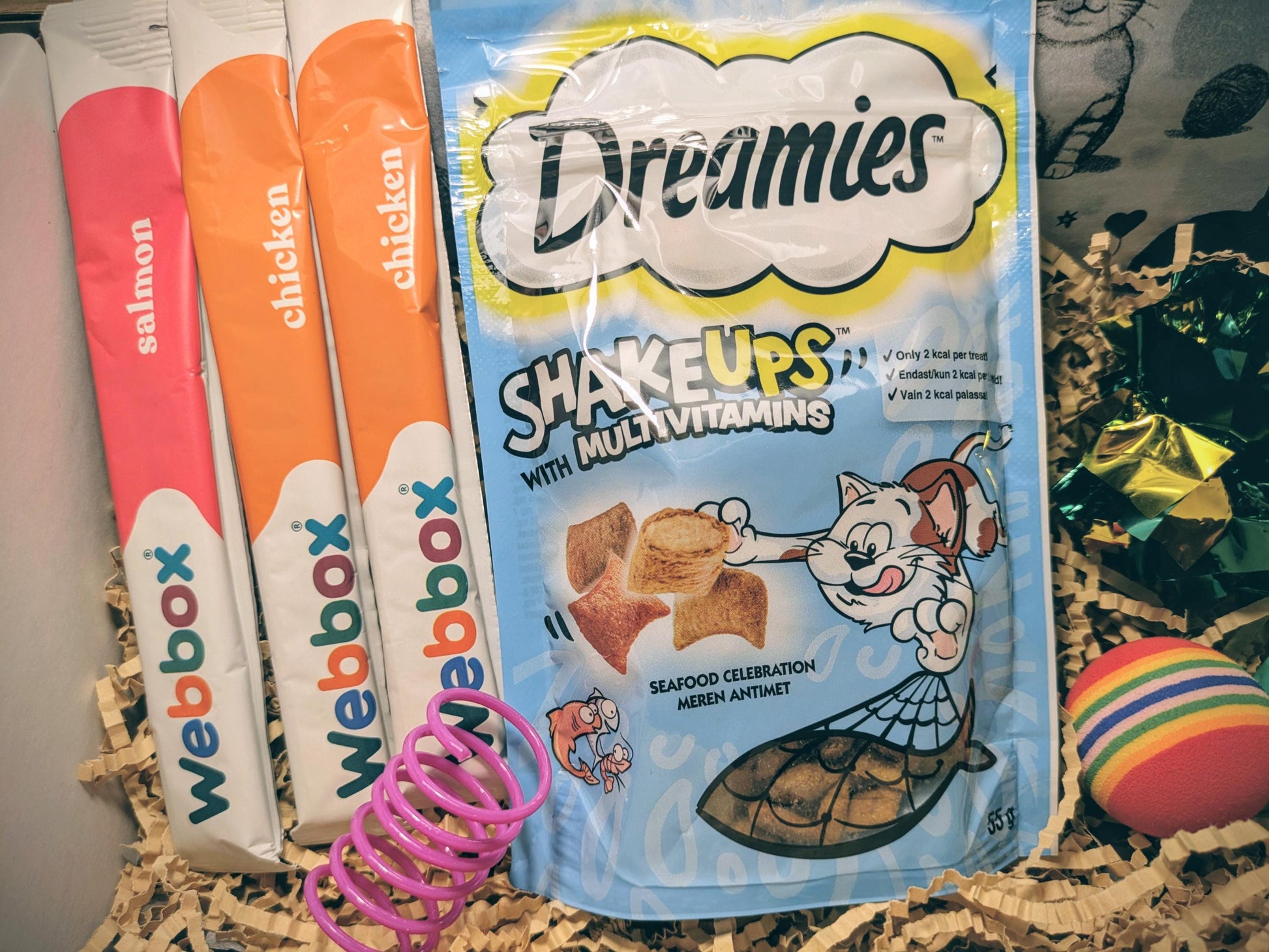 Starter personalised cat treat box showing Dreamies Shake Ups multi-vitamin treats, Weebbox chicken treats, colorful cat.