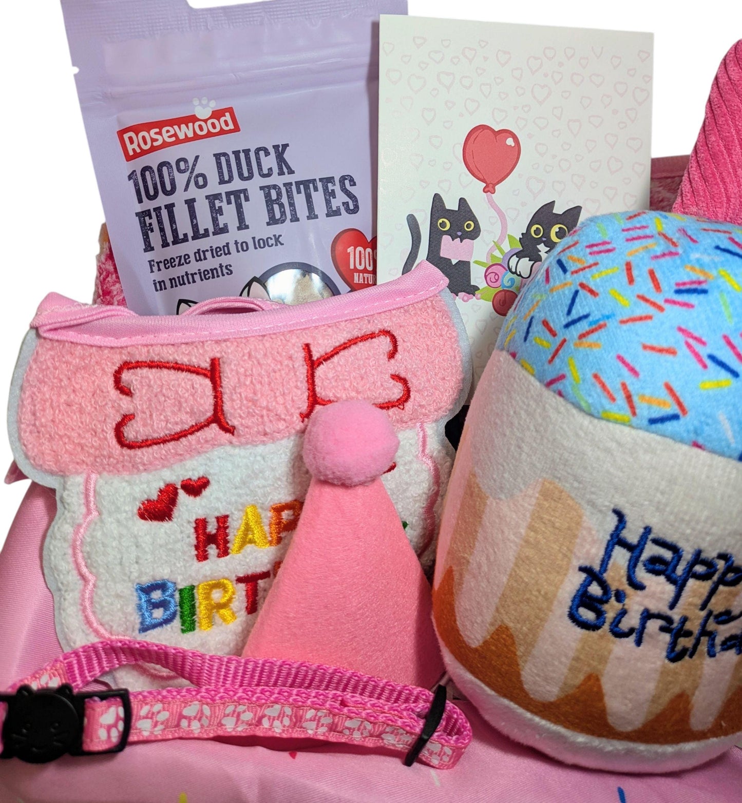 Pink birthday harness with bow and "Happy Birthday" text, pink party hat, blue sprinkle cupcake toy, duck fillet bites bag,.