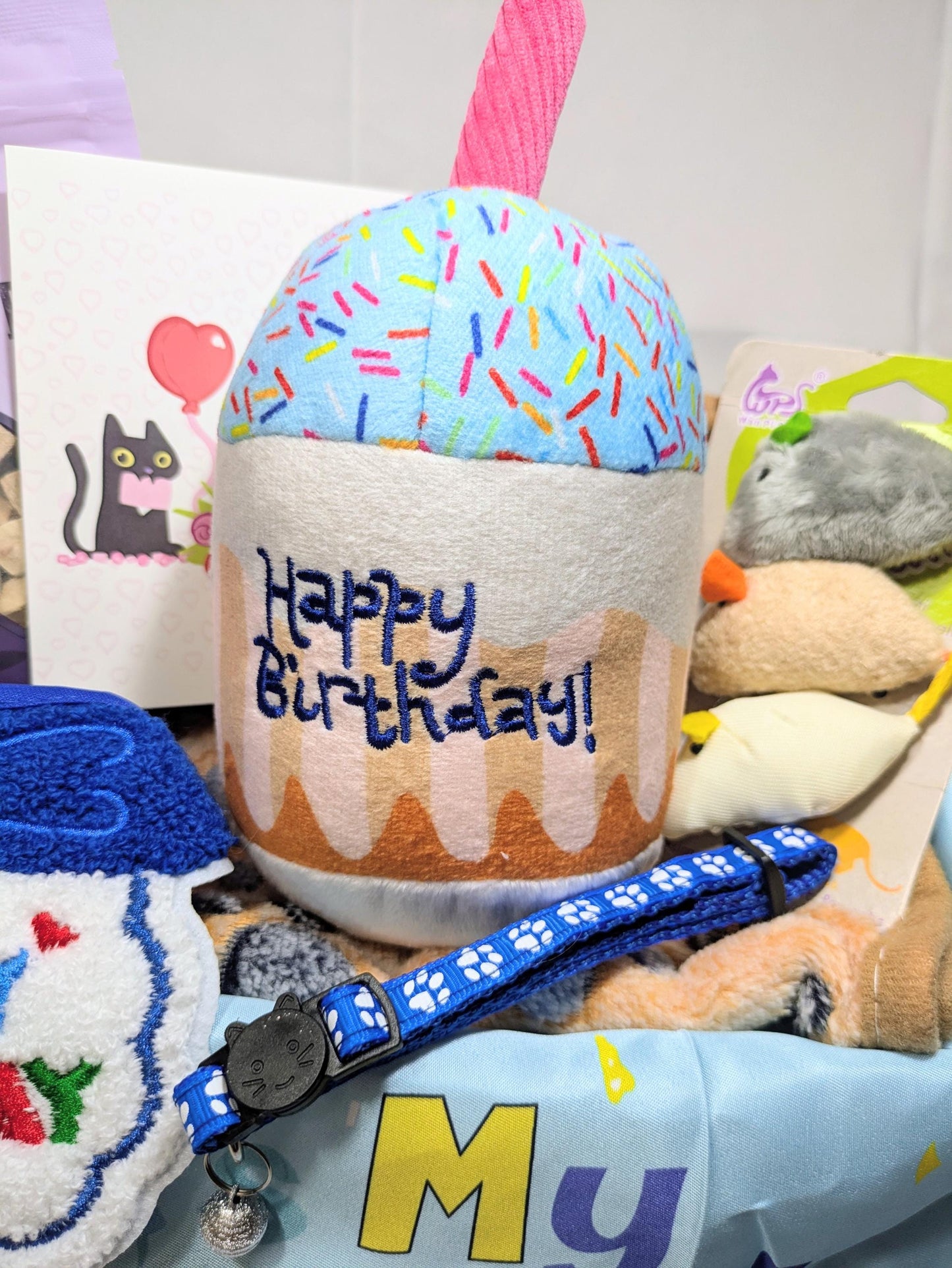 Handmade cat birthday gift box with cupcake treat, blue collar, toys, and colorful confetti design.