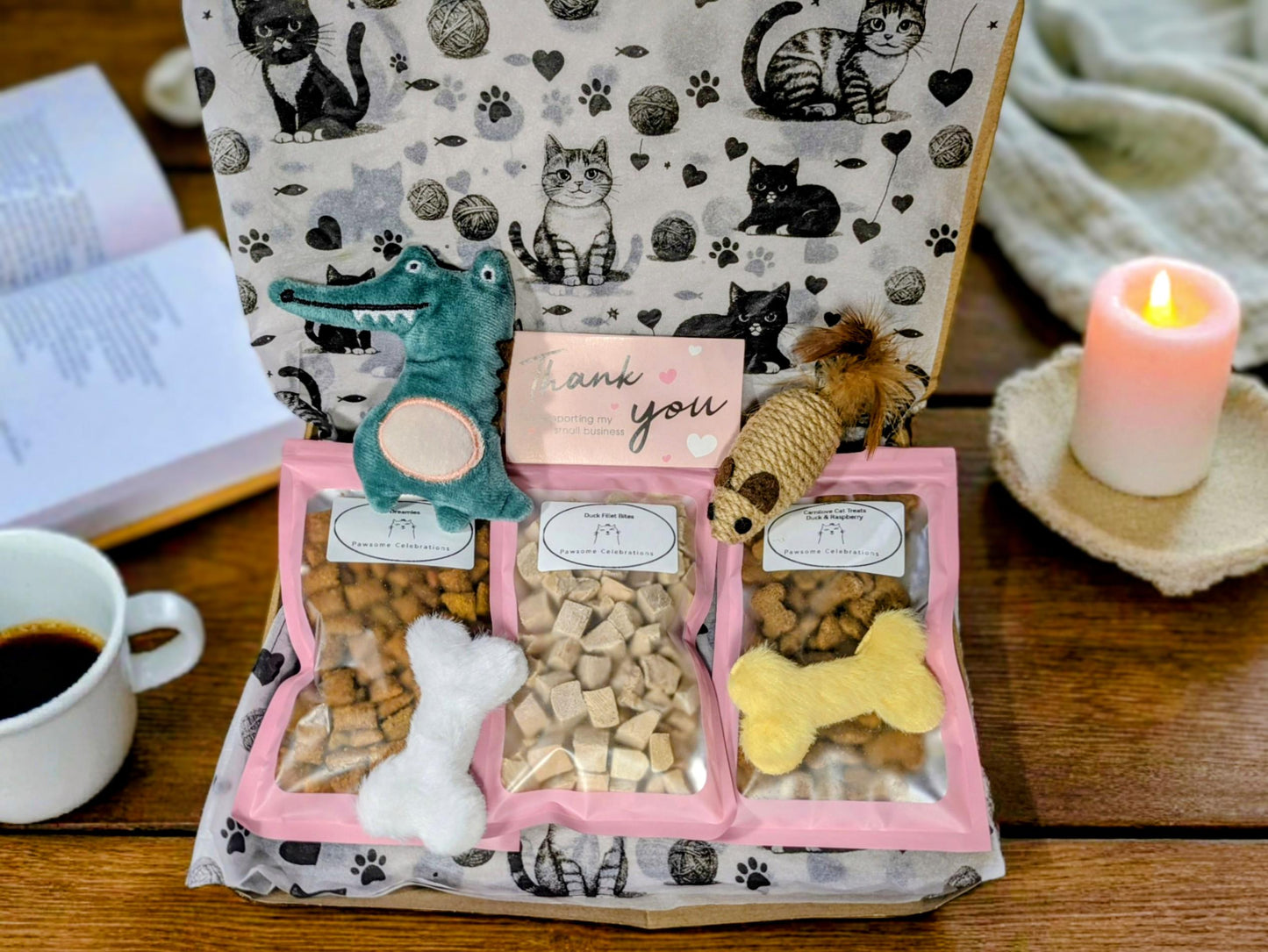 Open cat treat box with three sections holding white, beige, and yellow bone-shaped treats, plus two catnip toys shaped like .