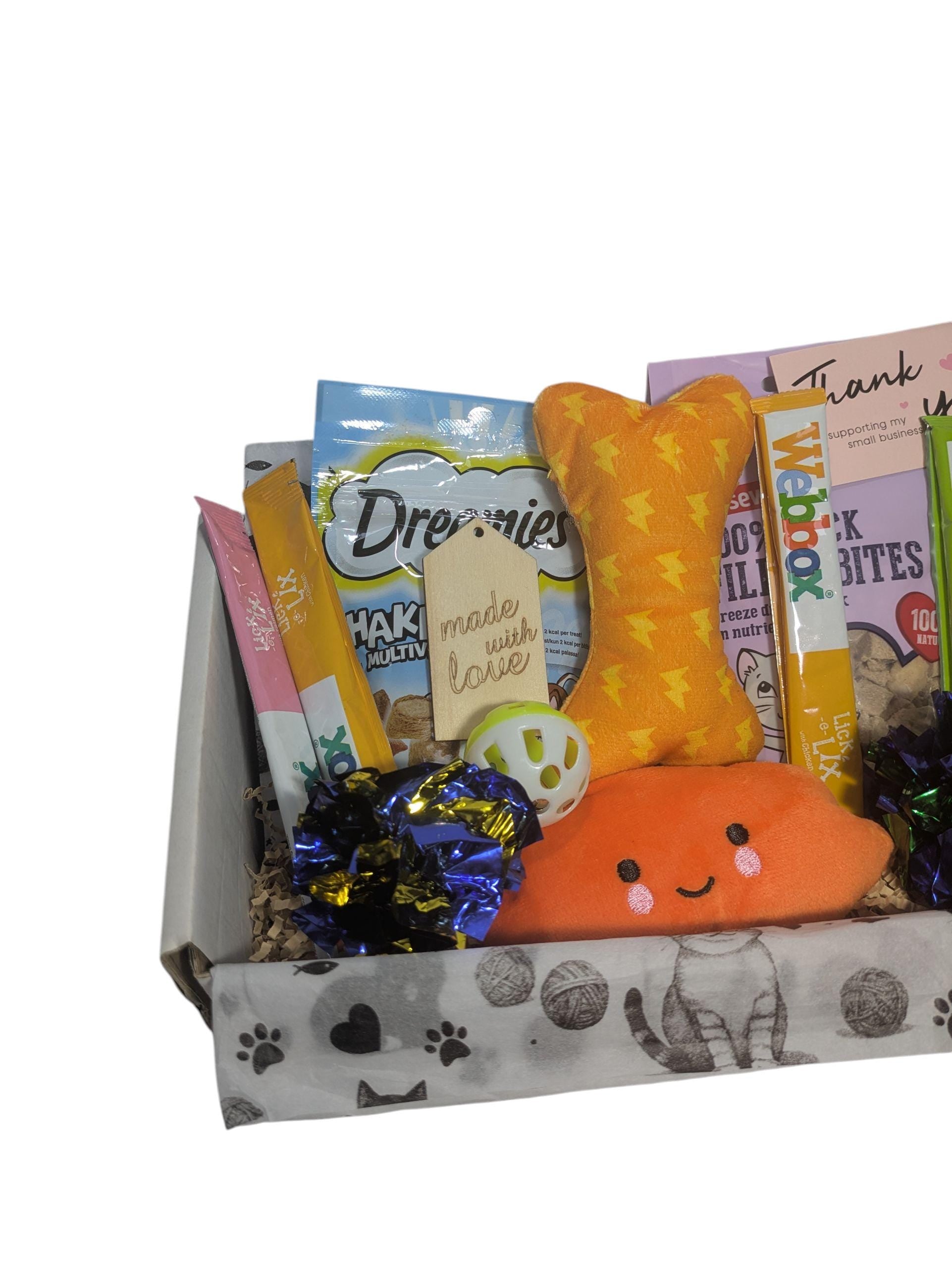 Eco-friendly cat gift box with orange bone toy, orange fish toy, treats, and blue pom-pom ball.