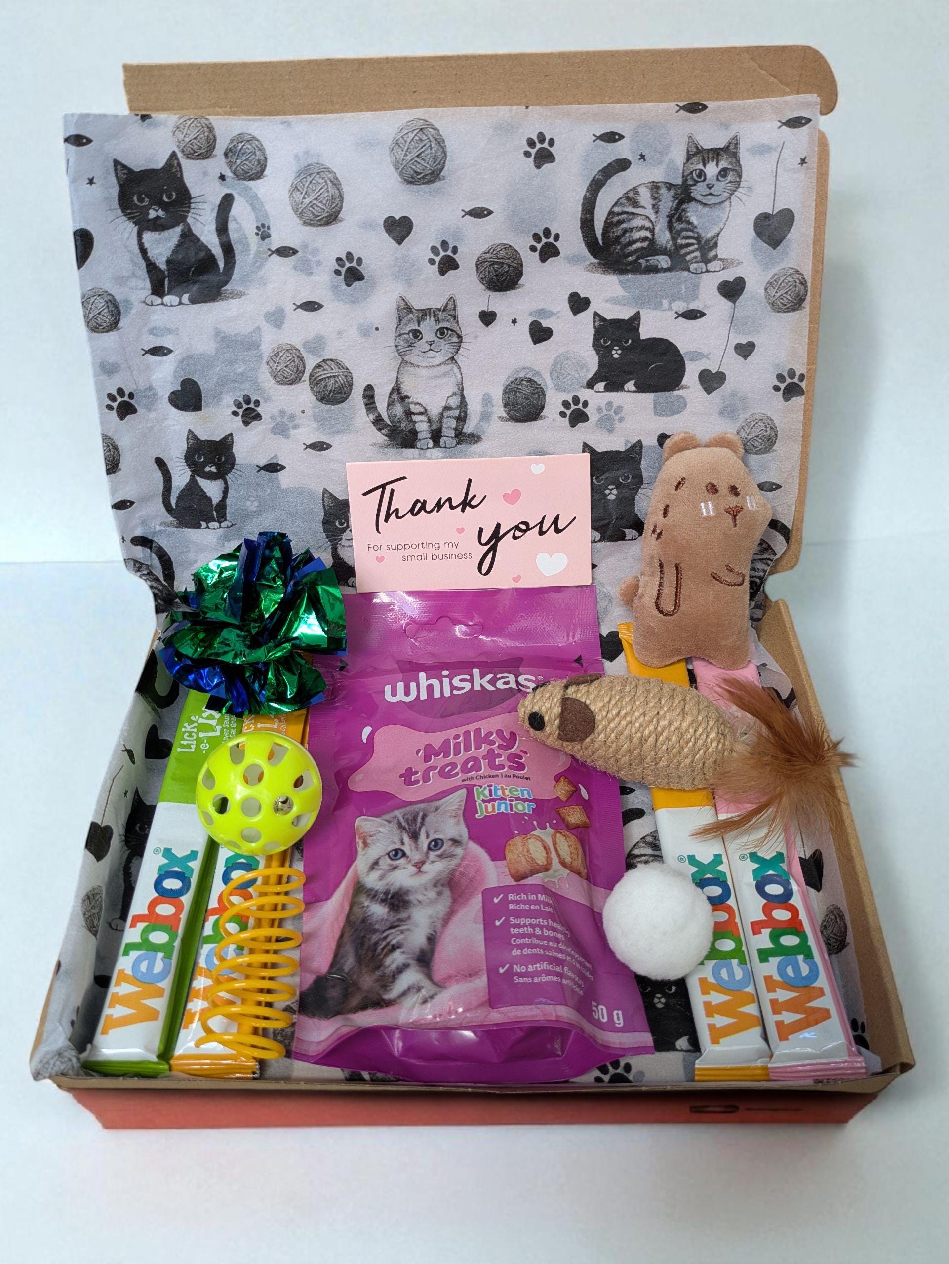 Open gift box with cat-themed lining, pink Whiskas kitten treats, colorful toys, and a thank you card.