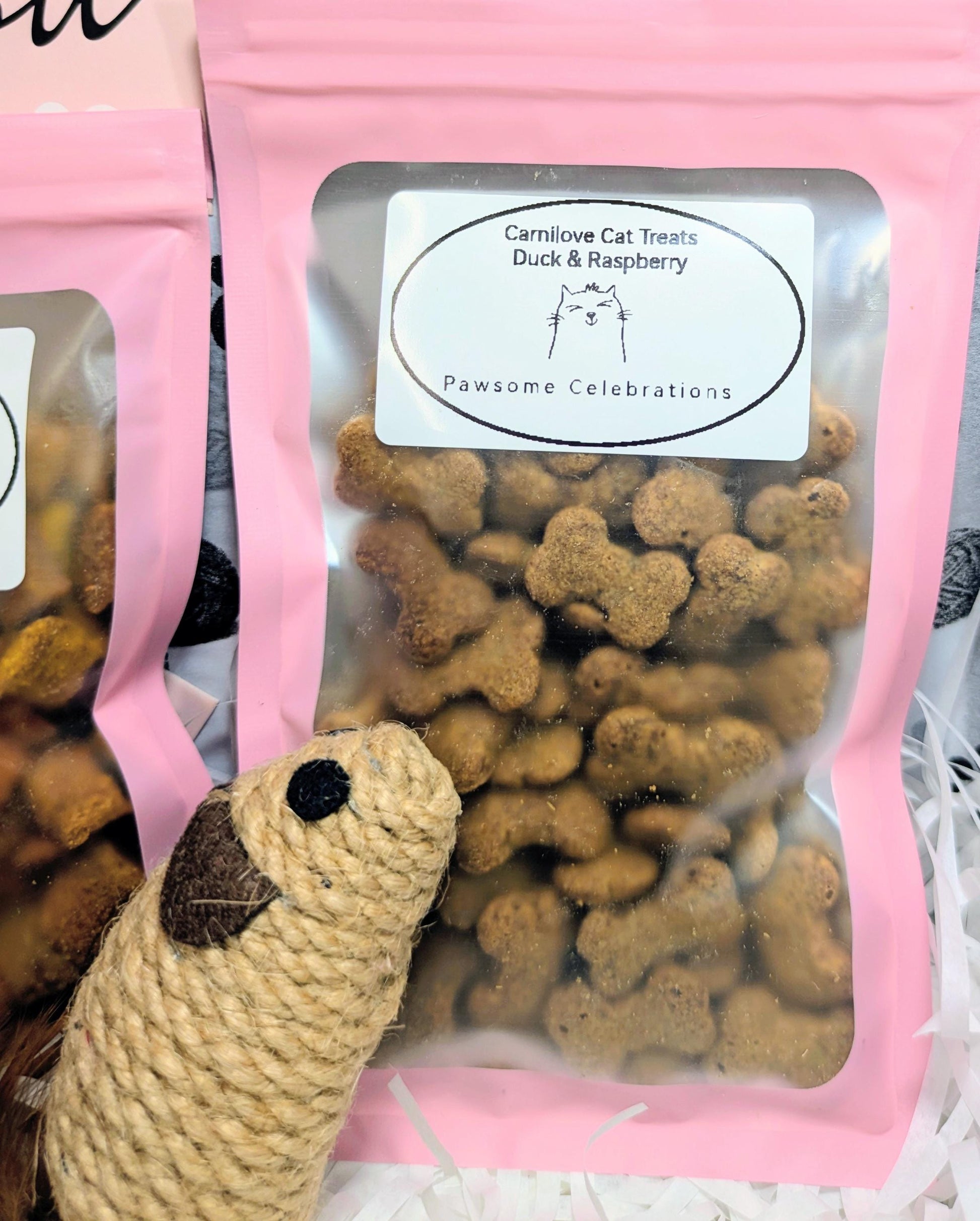 Pink resealable bag of duck and raspberry cat treats with a rope mouse toy in front.