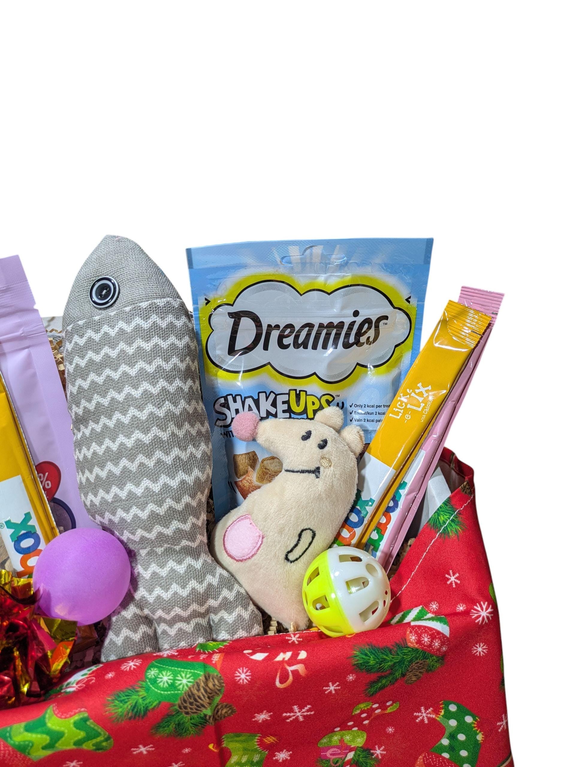 Festive red cat hamper filled with Dreamies treats, grey fish toy, plush mouse, and colorful cat toys.